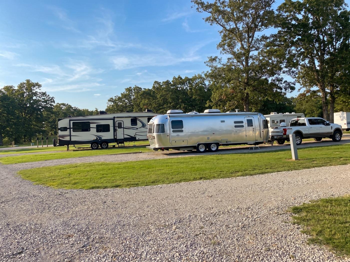Airstream trailer parked beside a fifth wheel at golden hour