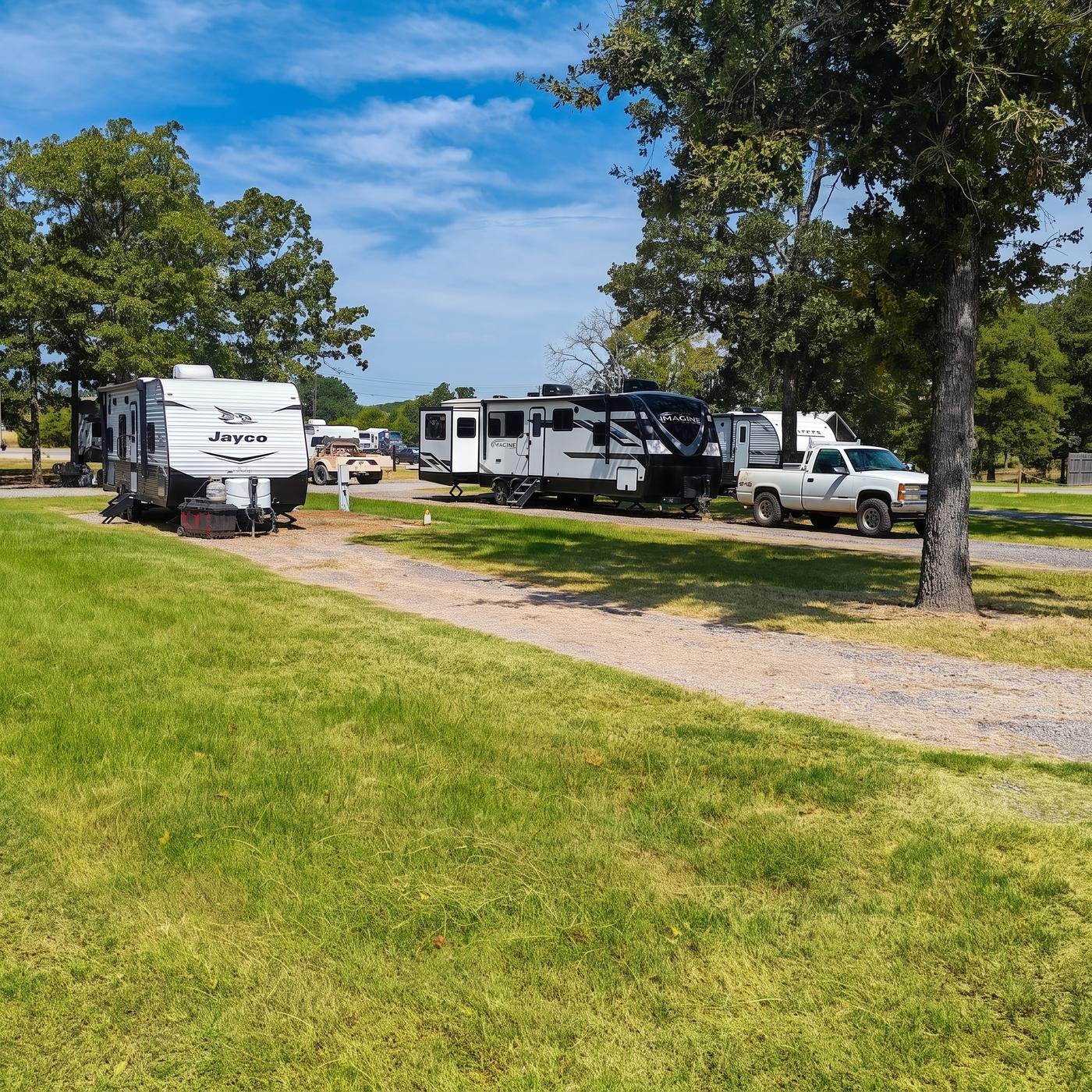 Travel trailers parked side by side under shade trees